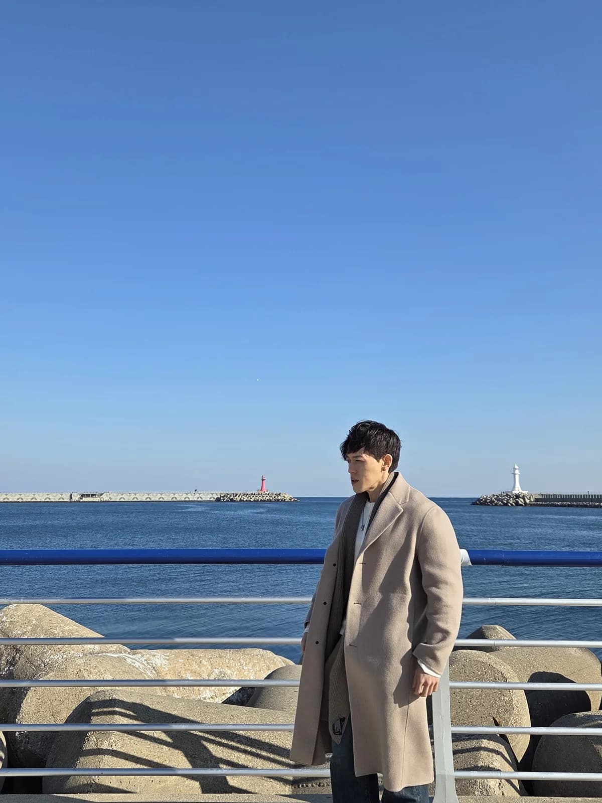 Founder standing by a blue seaside rail in a beige coat