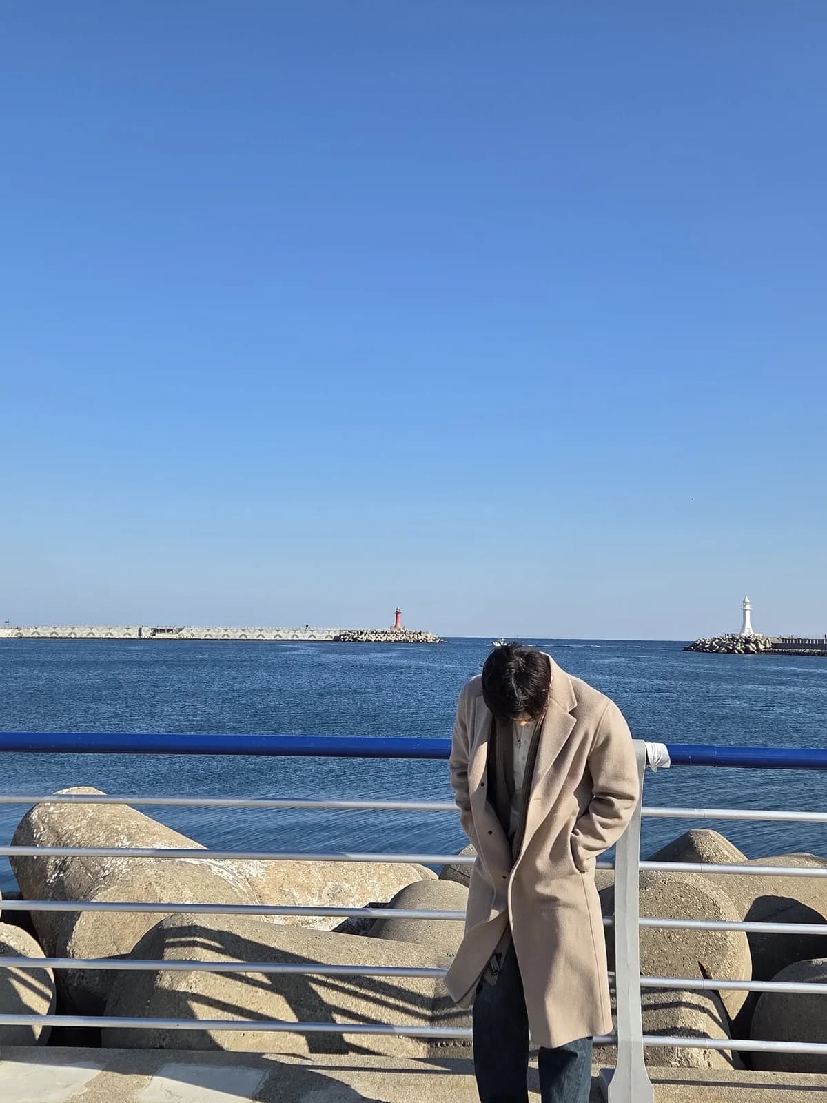 Founder looking down beside a blue seaside rail in a beige coat